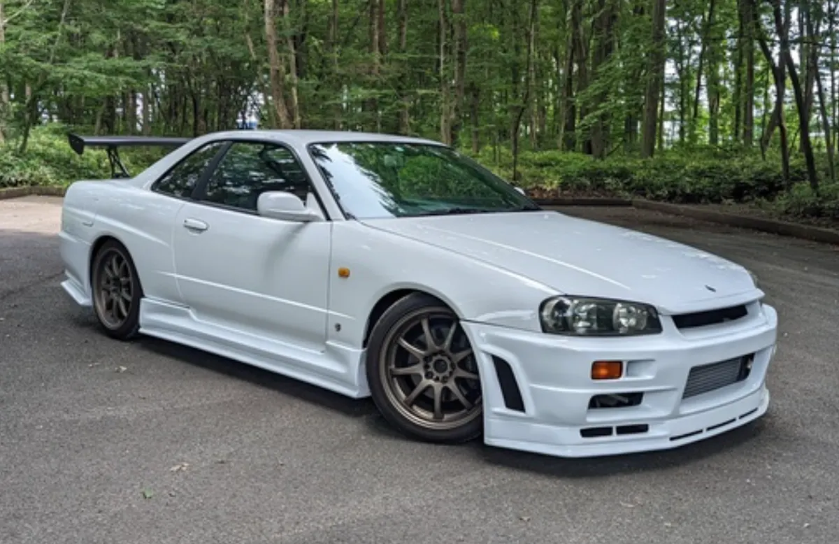 林道に停まる白のスカイラインクーペ（R34）。GTウイング付き